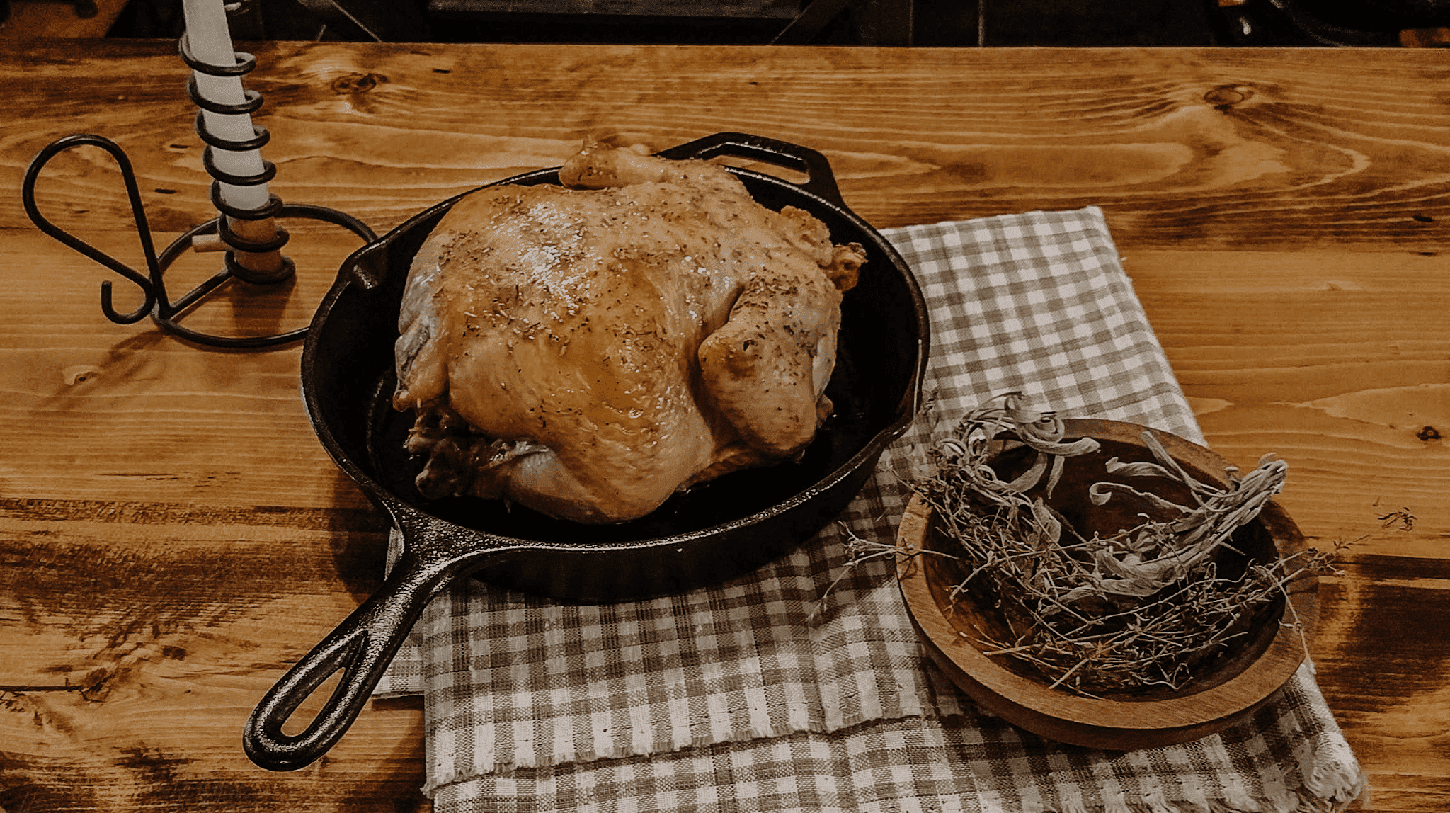 Whole Roast Chicken in pan on wooden table near candlestick and wooden bowl