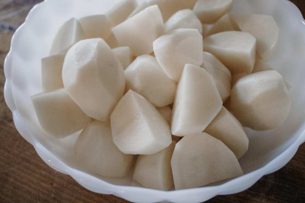 Cut potatoes in a white bowl on the table, ready to make Best Roasted Garlic Mashed Potatoes