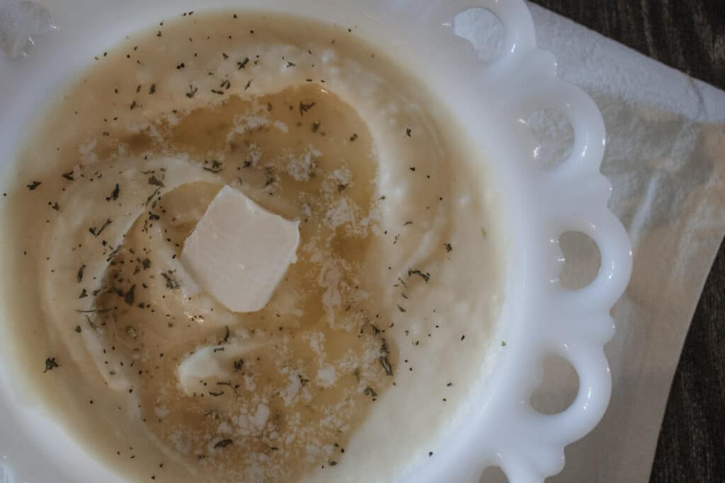 Best Roasted Garlic Mashed Potatoes in a white bowl with parsley and melted butter
